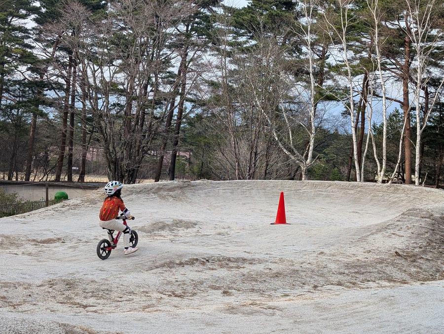 A child in a helmet riding a balance bike on the gravel trail-bike track at Fuji Subaru Land